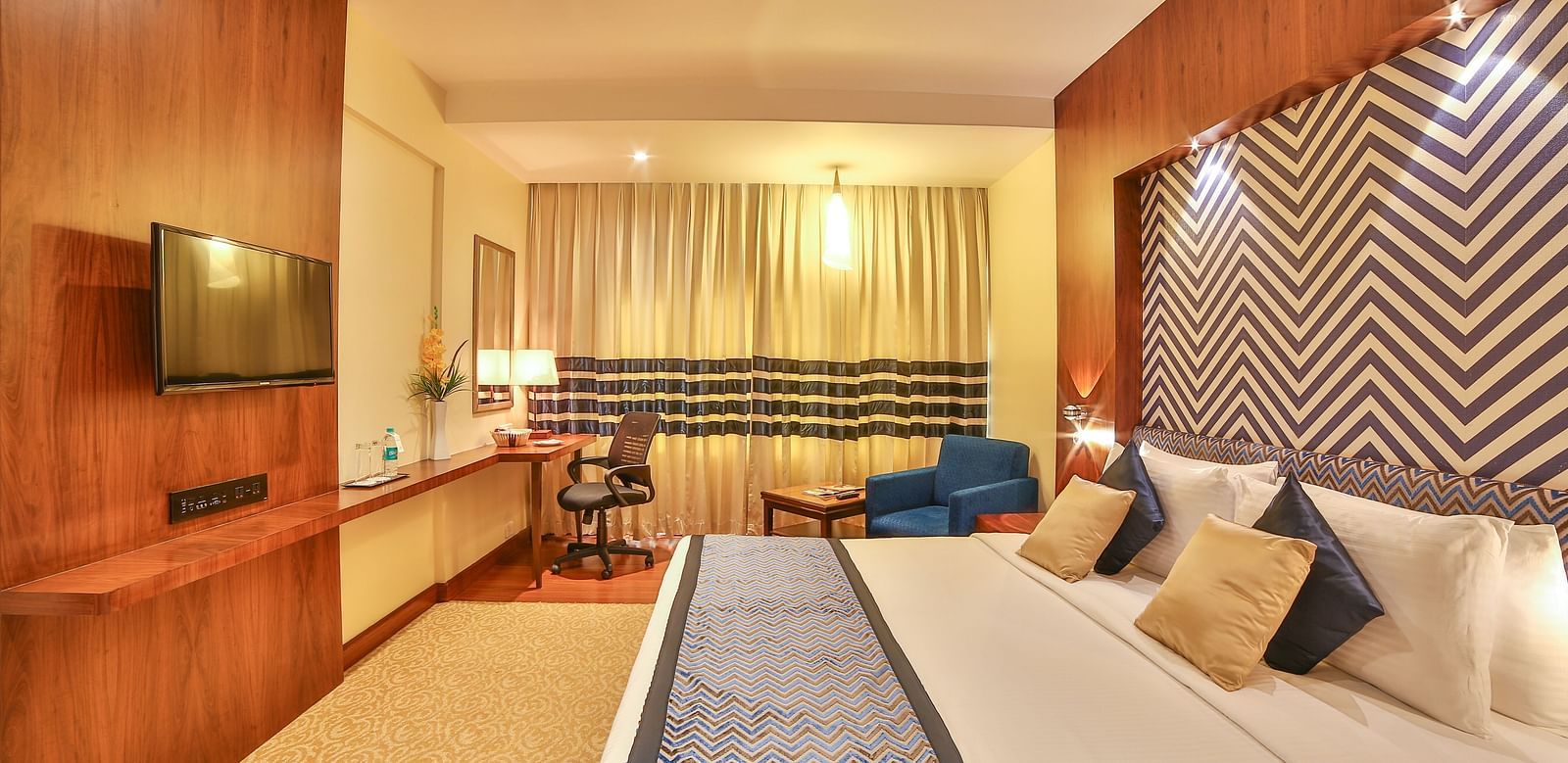 A spacious and modern hotel room with luxurious twin beds, a sofa, and sophisticated interior decor A grand hotel suite with an opulent red and white decor, large bed, and seating area, reflecting a traditional style at Sitara Luxury Hotel in Hyderabad nea