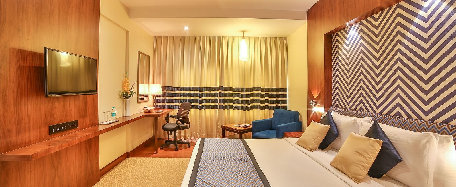A spacious and modern hotel room with luxurious twin beds, a sofa, and sophisticated interior decor A grand hotel suite with an opulent red and white decor, large bed, and seating area, reflecting a traditional style at Sitara Luxury Hotel in Hyderabad nea