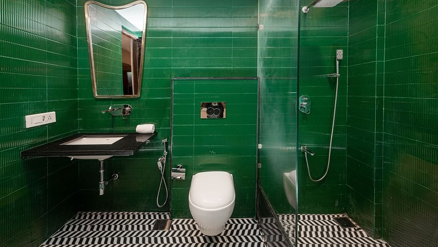 A modern washroom featuring sleek fittings, a large mirror, and stylish green accents at Crescent Resort, Goa