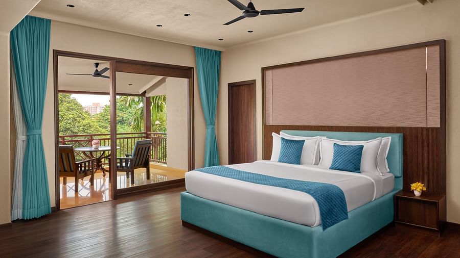 Super Deluxe Room with Balcony with a large bed, blue bedding, and a balcony with outdoor seating overlooking greenery at DGV Resort by Treat, Silvassa.