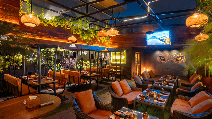 An indoor restaurant space with hanging lights, cushioned seating and decorated tables in a greenery setting at Infiniti Hotel, Indore.