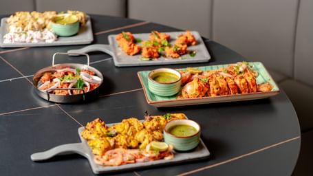Table laden with multiple platters of appetizers and dipping sauces | Pravasa Hotel, Vijayapura