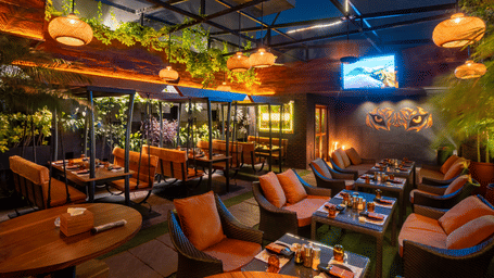 An indoor restaurant space with hanging lights, cushioned seating and decorated tables in a greenery setting at Infiniti Hotel, Indore.