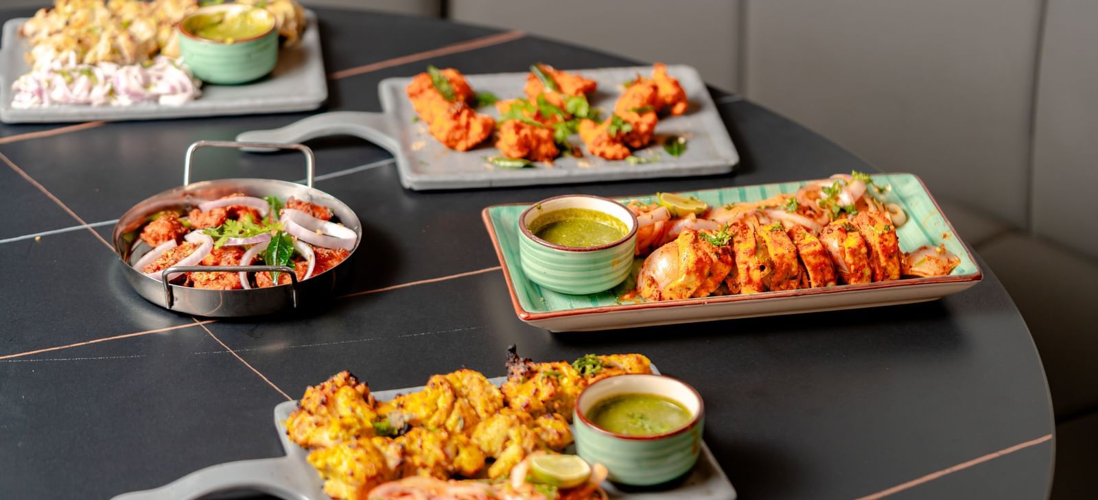 Table laden with multiple platters of appetizers and dipping sauces | Pravasa Hotel, Vijayapura