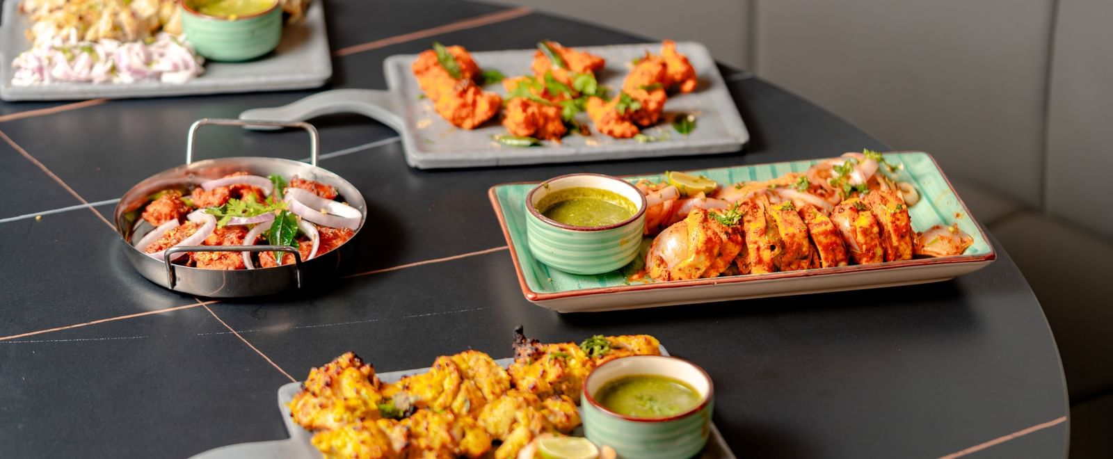 Table laden with multiple platters of appetizers and dipping sauces | Pravasa Hotel, Vijayapura