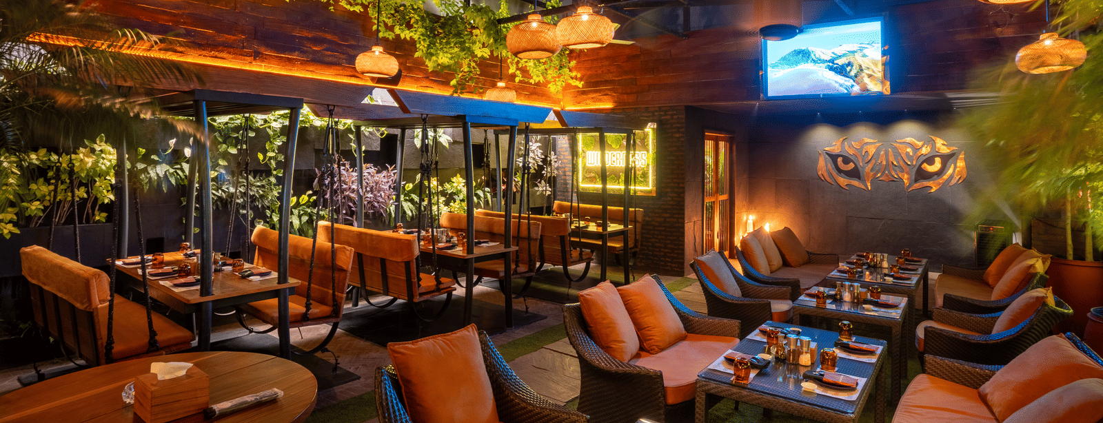 An indoor restaurant space with hanging lights, cushioned seating and decorated tables in a greenery setting at Infiniti Hotel, Indore.