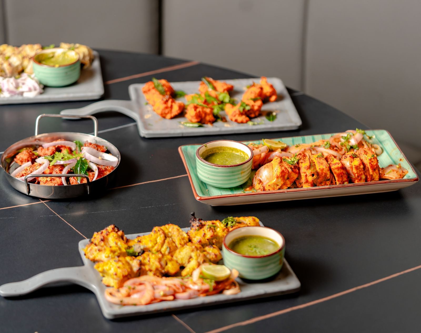 Table laden with multiple platters of appetizers and dipping sauces | Pravasa Hotel, Vijayapura