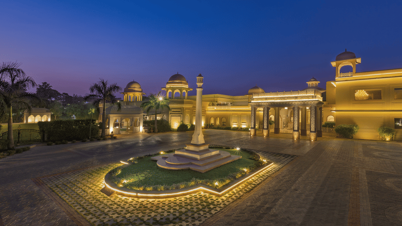 Front view of Heritage Village Resorts & Spa, Manesar with driveway, central fountain, and landscaped entrance in night.