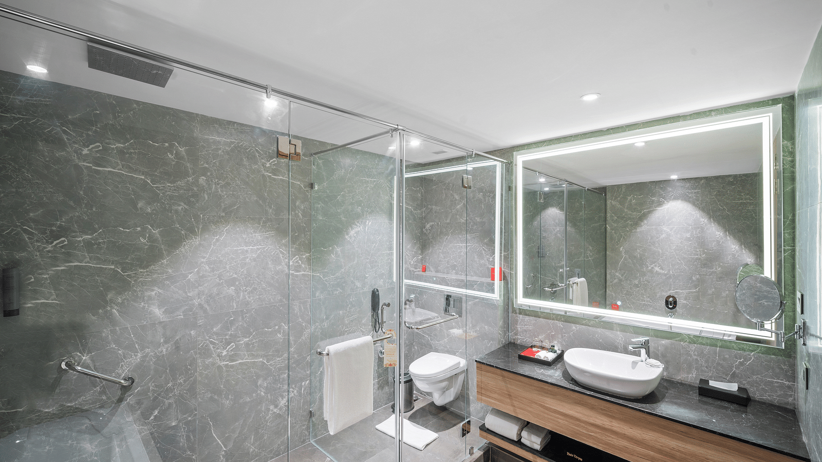 An ensuite bathroom with a shower area, a sink, and a wall-mounted mirror - Grand Vijaywada by GRT Hotels