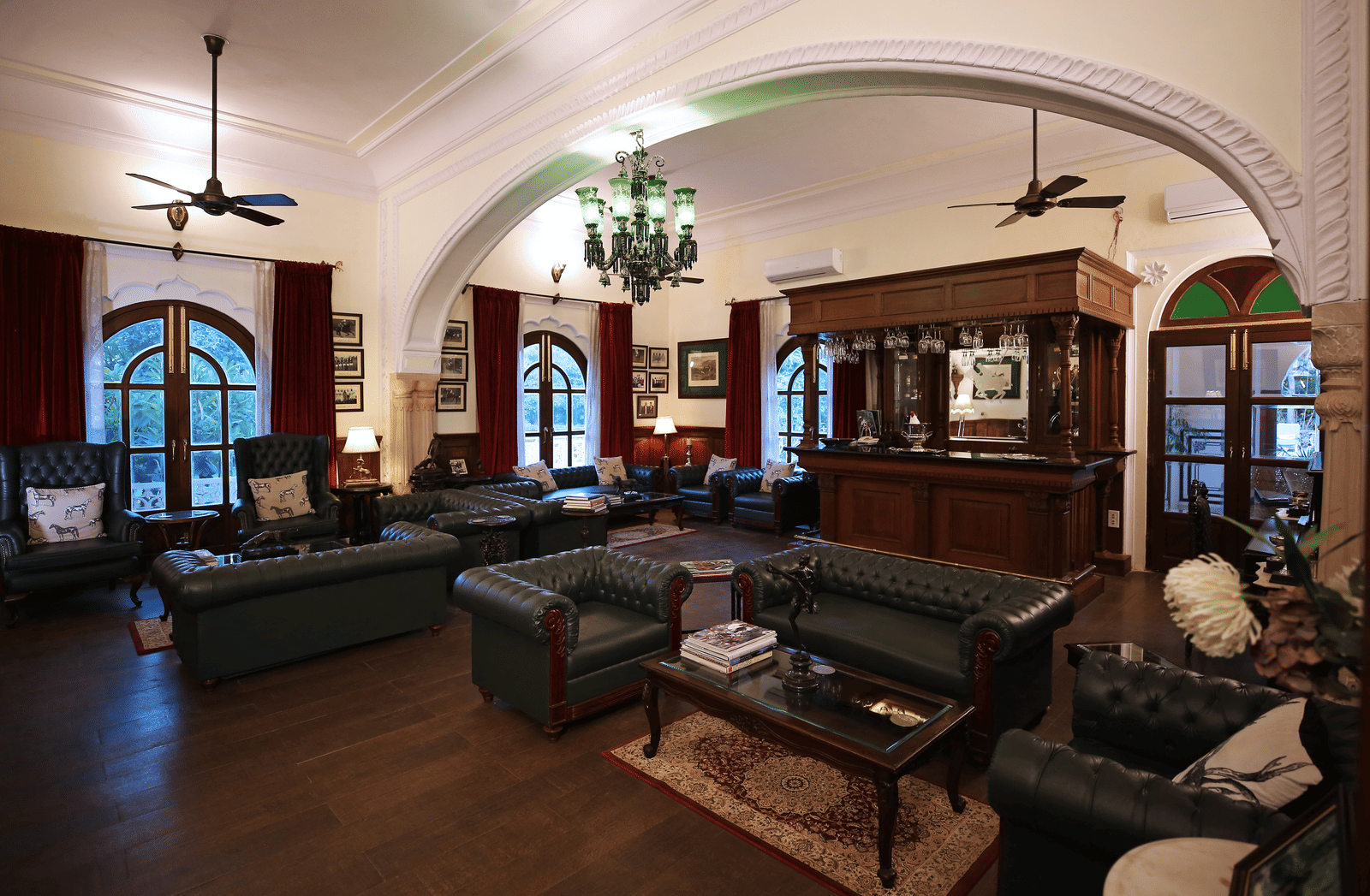 A grand living room with vintage sofas, chandeliers, and arched windows offering natural light - Khas Bagh, Jaipur.