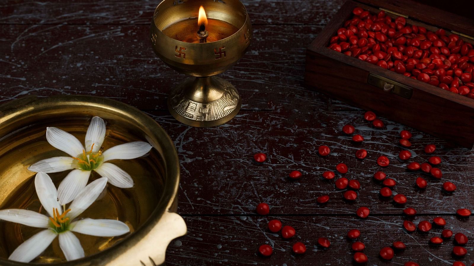 A dimly lit scene with a lit candle in a golden holder, a bowl of floating white flowers, and scattered red berries.