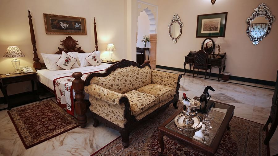 An opulent hotel bedroom with a four-poster bed and a traditional patterned sofa - Khas Bagh, Jaipur.