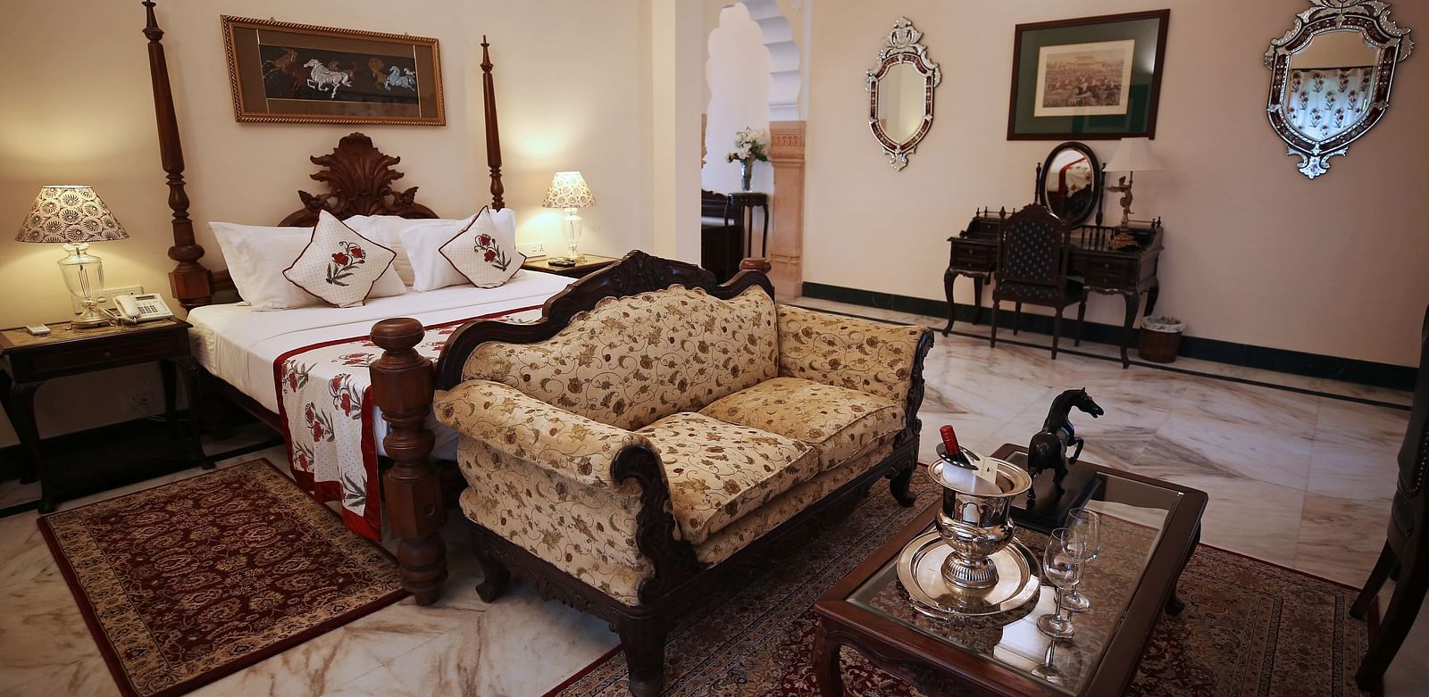 An opulent hotel bedroom with a four-poster bed and a traditional patterned sofa - Khas Bagh, Jaipur.