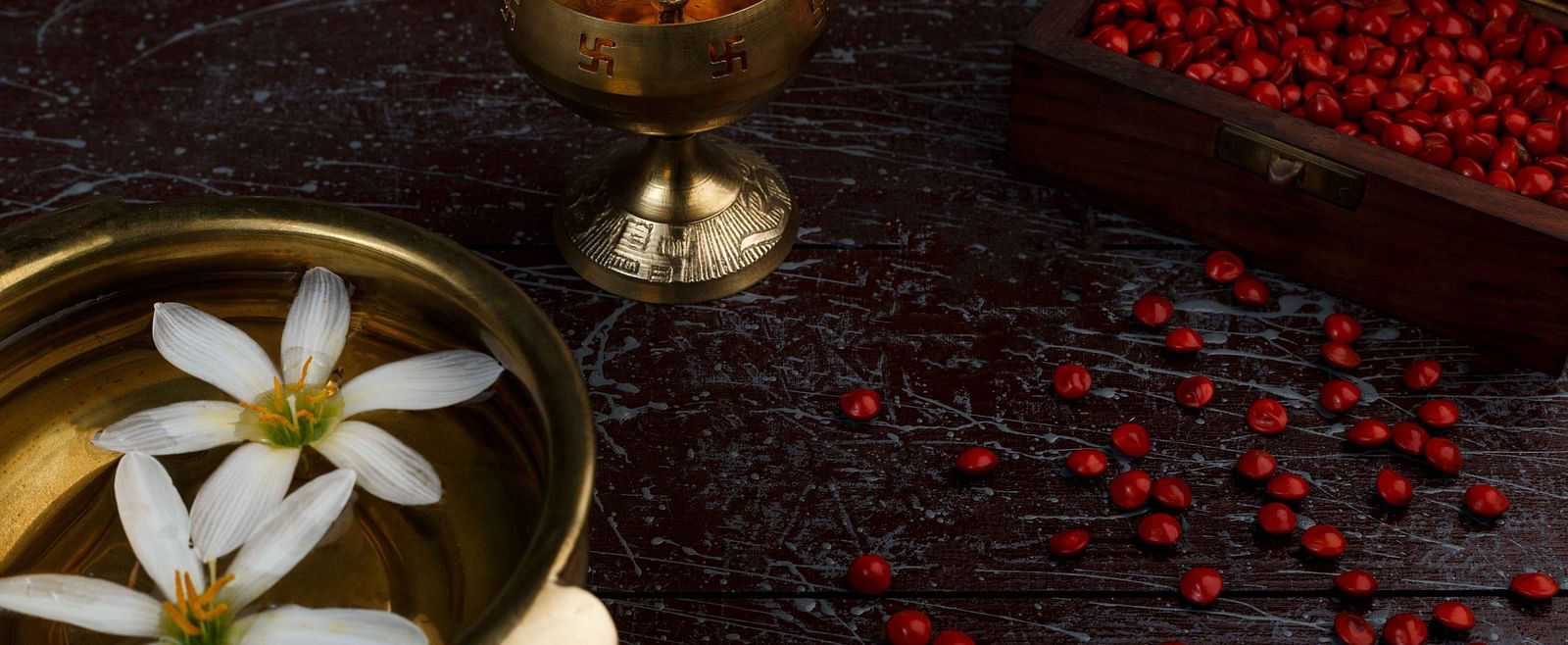 A dimly lit scene with a lit candle in a golden holder, a bowl of floating white flowers, and scattered red berries.