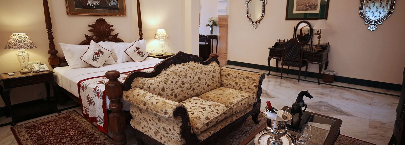 An opulent hotel bedroom with a four-poster bed and a traditional patterned sofa - Khas Bagh, Jaipur.