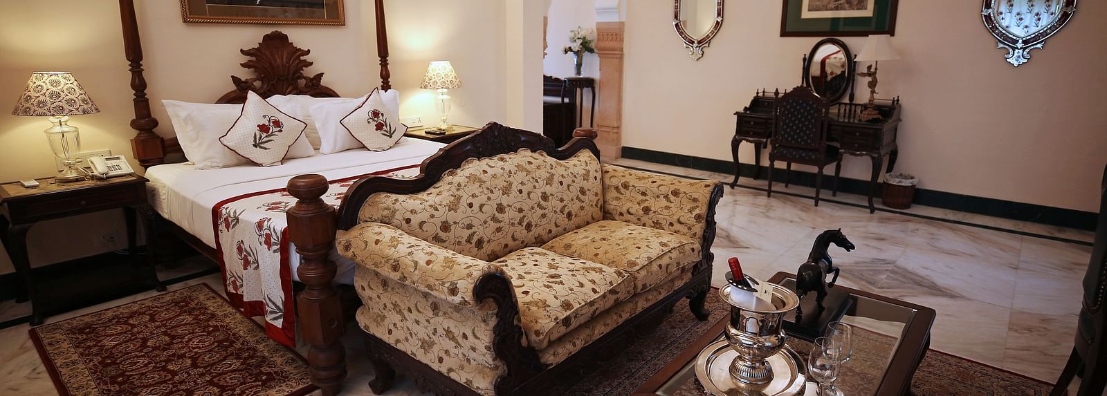 An opulent hotel bedroom with a four-poster bed and a traditional patterned sofa - Khas Bagh, Jaipur.
