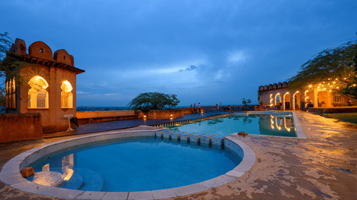 Hill Fort Kesroli 14th Century Alwar - view of two adjoined round swimming pools with an illuminated building structure in the background