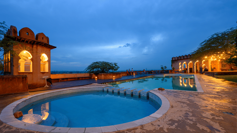Hill Fort Kesroli 14th Century Alwar - view of two adjoined round swimming pools with an illuminated building structure in the background