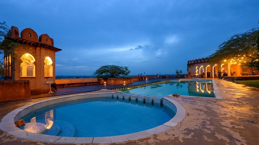 Hill Fort Kesroli 14th Century Alwar - view of two adjoined round swimming pools with an illuminated building structure in the background