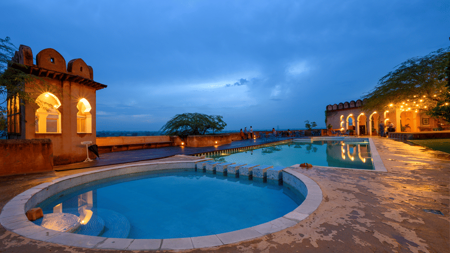 Hill Fort Kesroli 14th Century Alwar - view of two adjoined round swimming pools with an illuminated building structure in the background