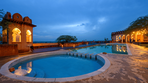 Hill Fort Kesroli 14th Century Alwar - view of two adjoined round swimming pools with an illuminated building structure in the background