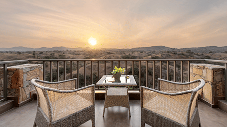 2 cosy wicker chairs sit on a balcony overlooking a breathtaking golden sunset across the distant horizon - Sajjan Bagh Resort and Spa, Kumbhalgarh