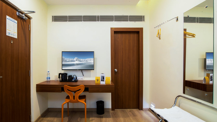 The Onyx guest room with a work desk and chair, wall-mounted television, wardrobe, door entry, and wooden floor layout.oom