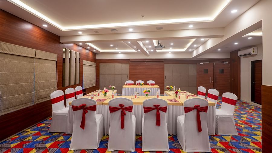 Conference room setup with a central table arrangement, chairs, and projector screen - Lords Eco Inn Shapar Rajkot