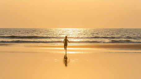 A far out view of a boy running towards the Arabian Sea on the shoreline with the sun's rays on the water on Benaulim Beach, Goa.