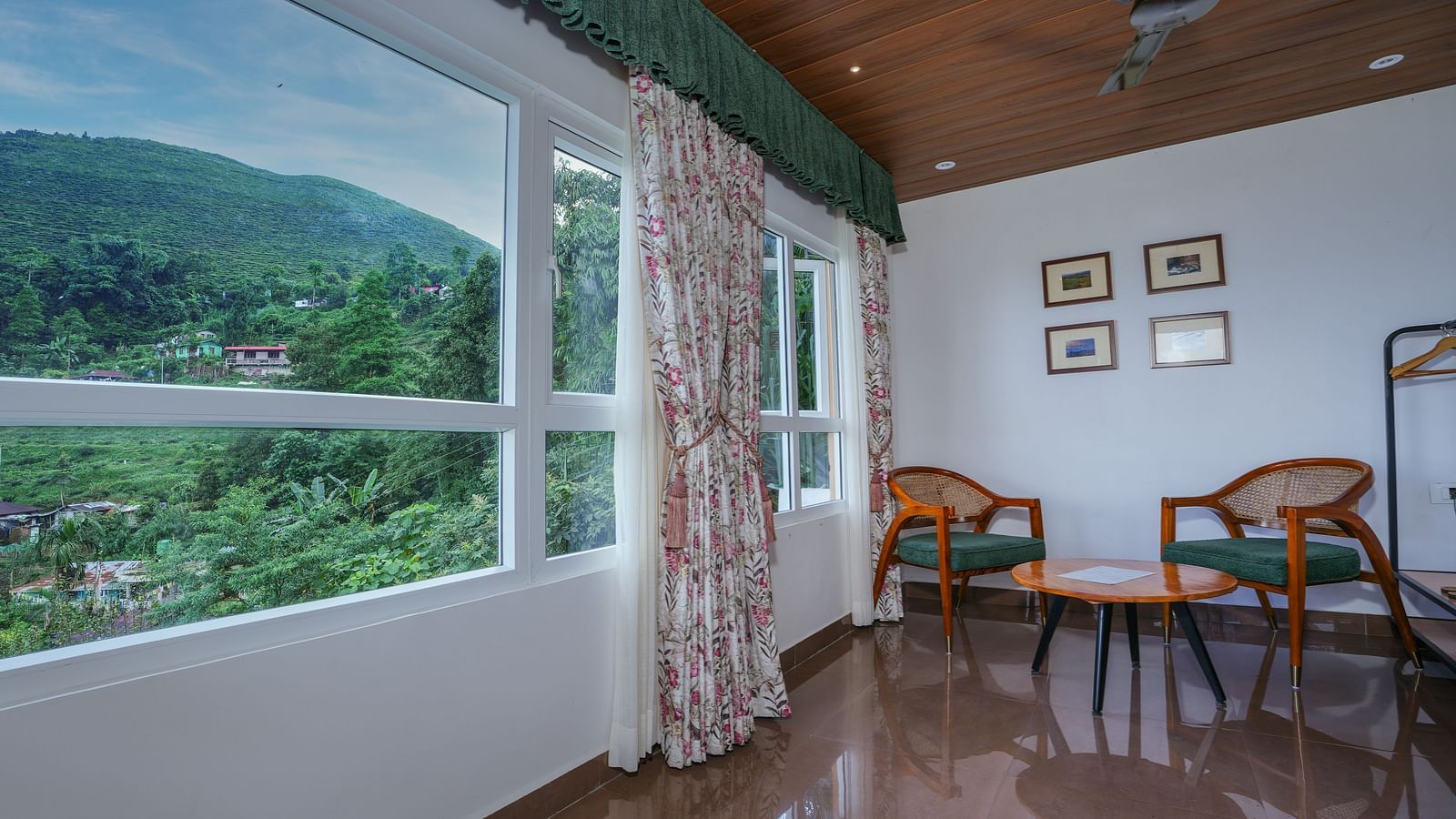 Large windows with nature views, comfortable seating, and a wooden table complement the spacious bed with side curtains and wooden furnishings