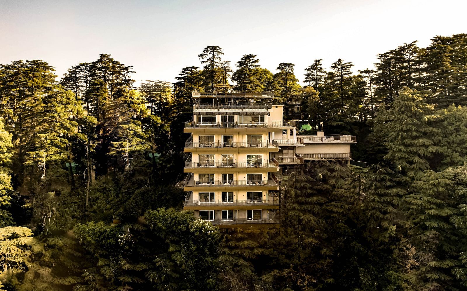 A wide-angle daytime shot of the facade of The Belvedere Himalayan Retreat in McLeodganj, set amidst lush jungle surroundings.