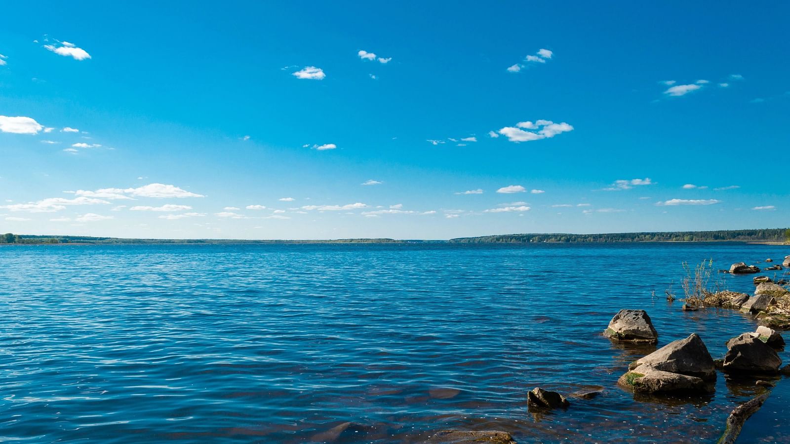 Lake with scattered clouds, rocks in foreground, mountain backdrop.
