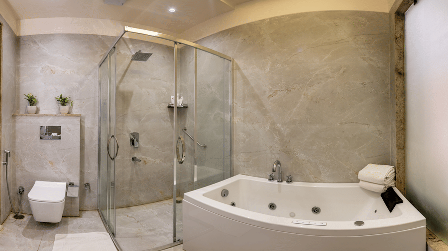 Elegant bathroom at Lords Inn Sangam, Bhopal featuring a jacuzzi tub, glass shower enclosure, toilet, and polished marble flooring.