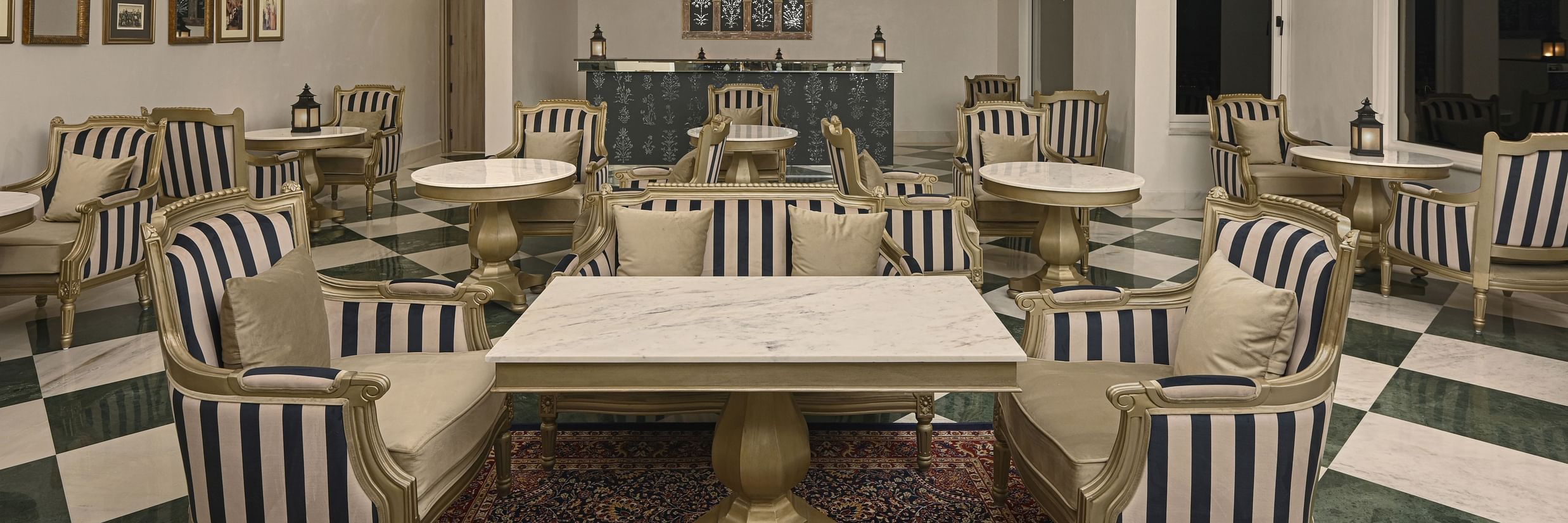 Interior of a restaurant at Khas Mahal by Fateh Collection, Udaipur with tables and chairs arranged for dining, featuring striped upholstery and ceiling decorations.