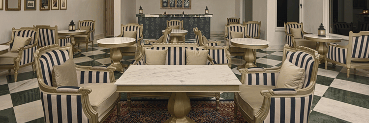 Interior of a restaurant at Khas Mahal Suites, Udaipur with tables and chairs arranged for dining, featuring striped upholstery and ceiling decorations.
