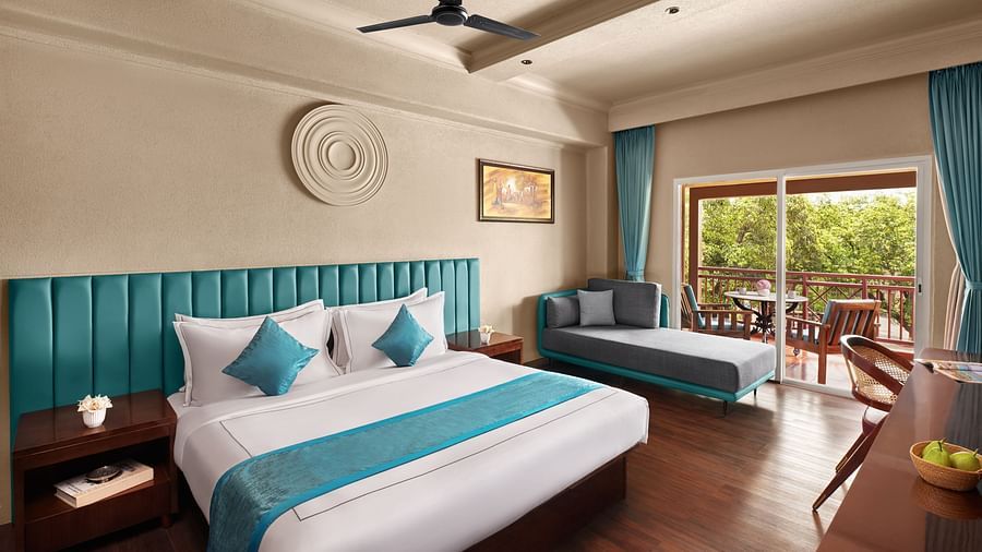 Executive Room with Balcony featuring a large bed, a chaise lounge, and a balcony overlooking lush scenery at DGV Resort by Treat, Silvassa.