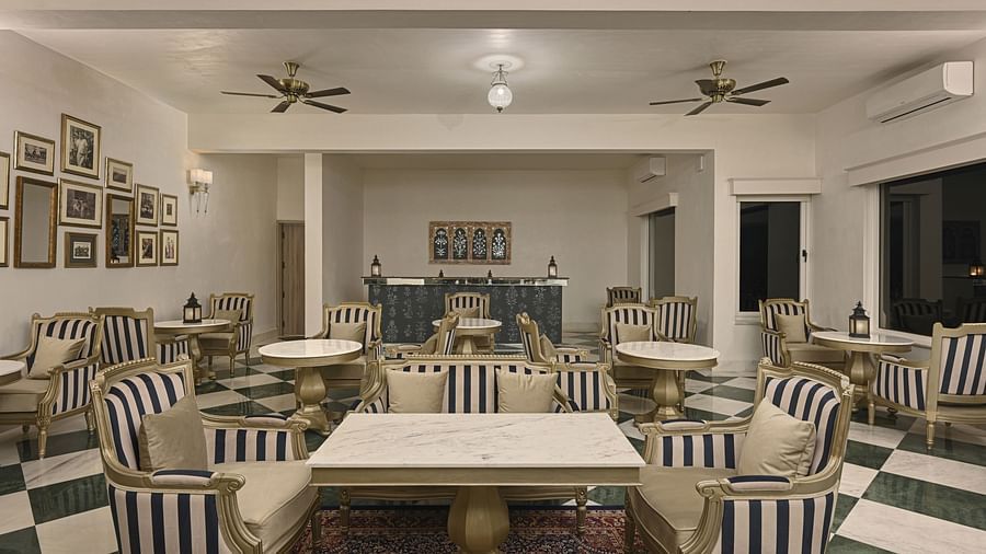 Interior of a restaurant at Khas Mahal by Fateh Collection, Udaipur with tables and chairs arranged for dining, featuring striped upholstery and ceiling decorations.