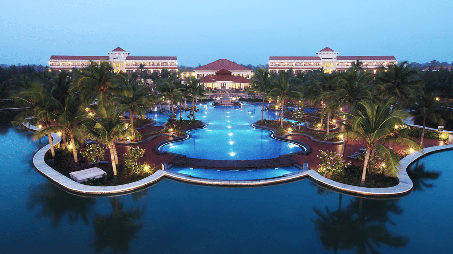 Ocean Spray resort in ECR, Pondicherry featuring a large lagoon-style swimming pool surrounded by palm trees and luxury villas at dusk.