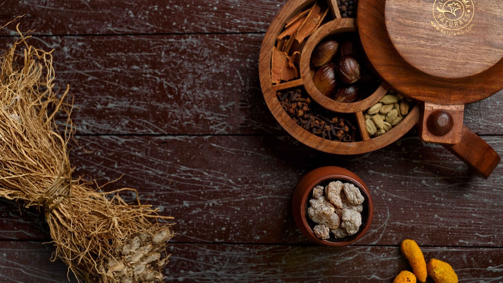 A top-down view of various dry goods, possibly spices or grains, arranged in wooden bowls and on a dark surface with scattered straw.
