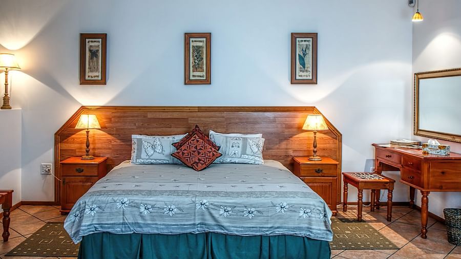 Image of a queen size bed with a white bedsheet and a side table with a stool - Stone Wood Mountain Resort, Dharamshala
