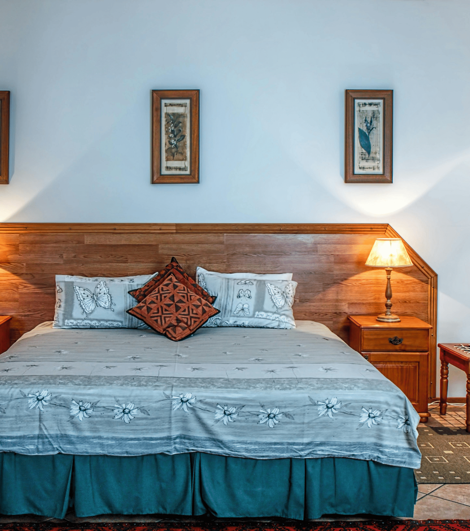 A cosy hotel bedroom with a large double bed, wooden headboard, two matching bedside tables and lamps, and three framed pictures.