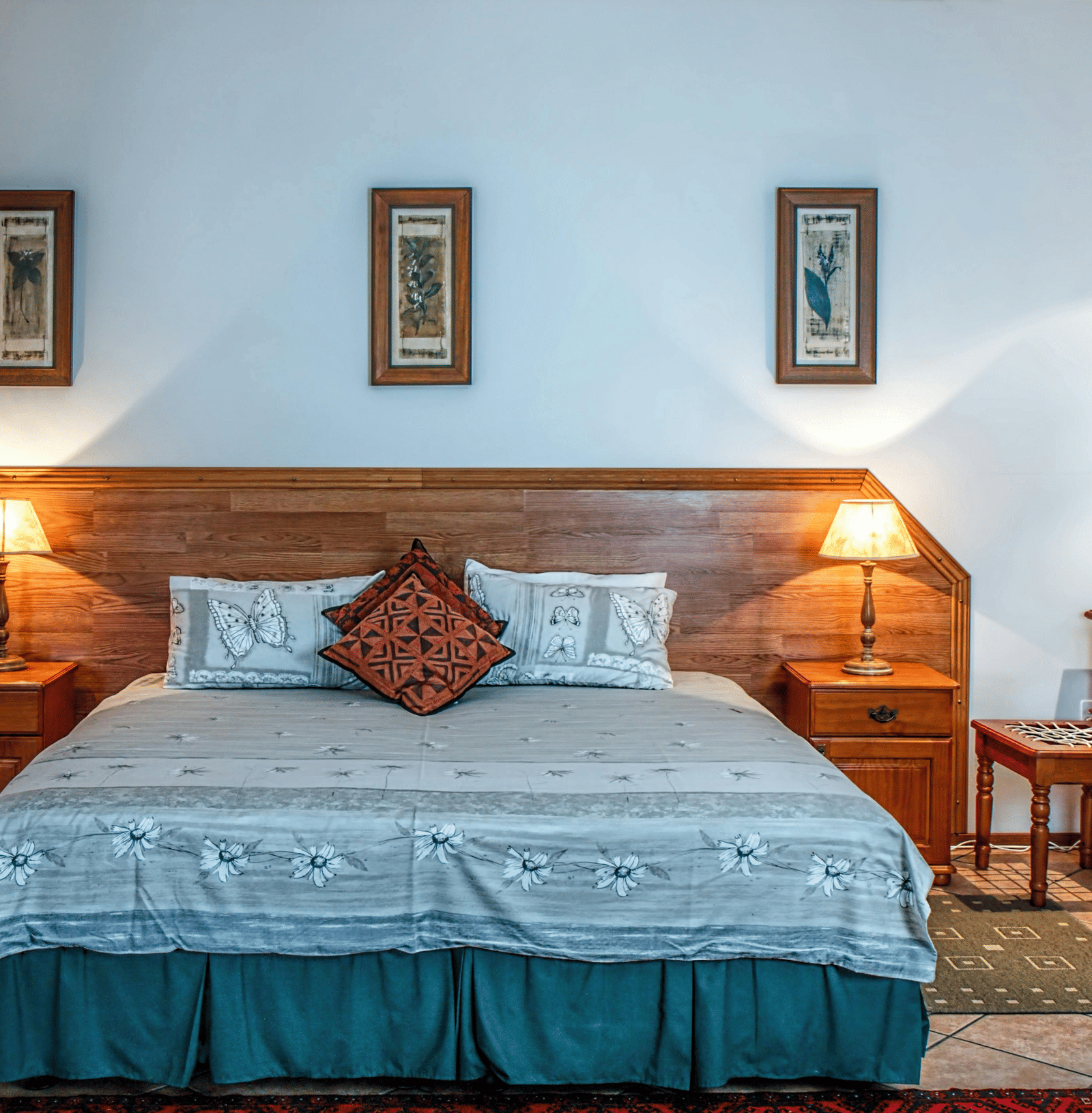 A cosy hotel bedroom with a large double bed, wooden headboard, two matching bedside tables and lamps, and three framed pictures.