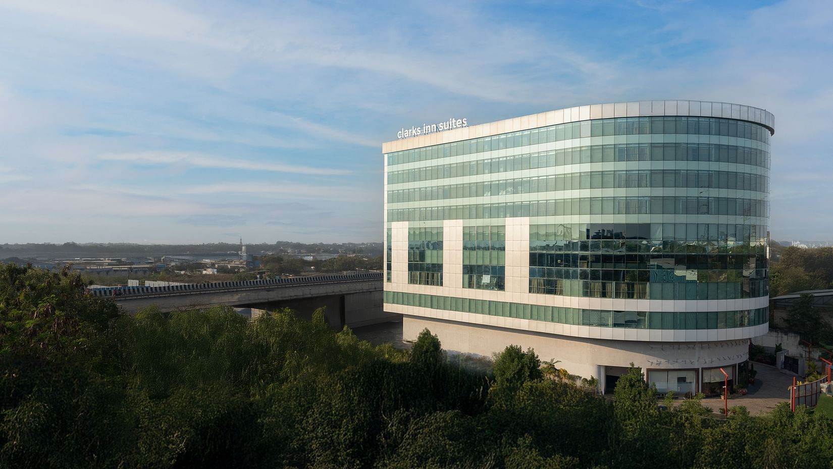 Daylight view of modern multi-storey glass hotel surrounded by landscaped greenery at Clarks Inn Suites, Hyderabad