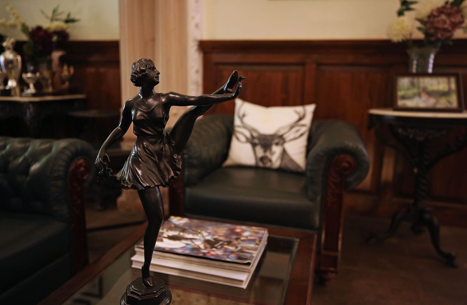 A dark green sofa with a decorative pillow featuring an animal design, and a dark statue of a person in a dimly lit room with wooden paneling - Khas Bagh