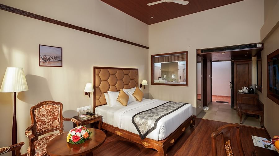 Room at Uday Backwater Resort featuring a plush bed with fresh linen and bed runner facing the TV mounted on the wall and a sitting space next to the floor lamp