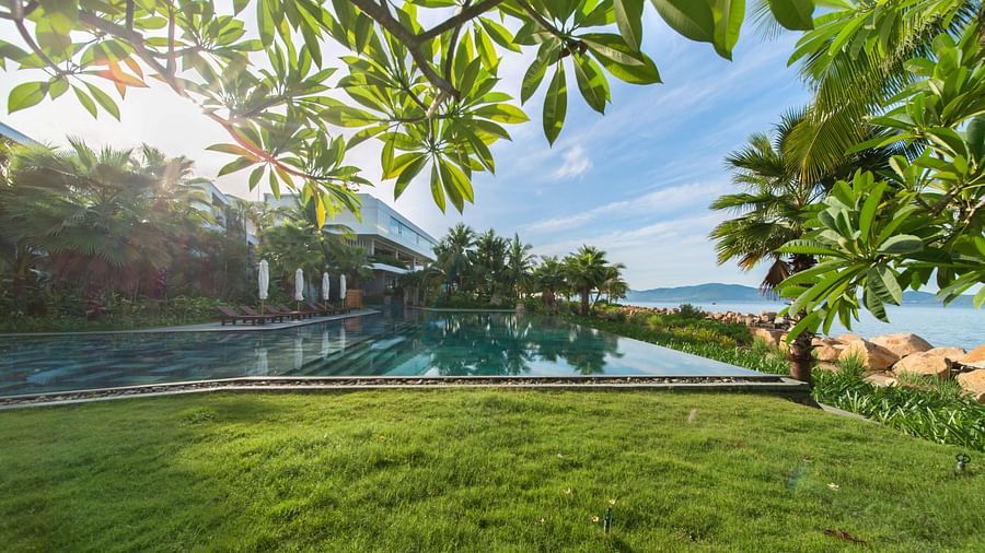 A well maintained pool with a well maintained garden by the side seen during a bright sunny day - Alibu Resort Nha trang