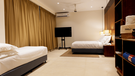 Hotel room at SUKAVI with 2 single beds, a wall-mounted television, and brown curtains covering the window.