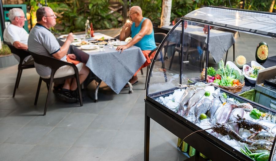 Fresh seafood display on ice with vegetables beside it, set in an open-air restaurant where guests are enjoying their meal in a lush, tropical setting at Uday Samudra Leisure Beach Hotel.