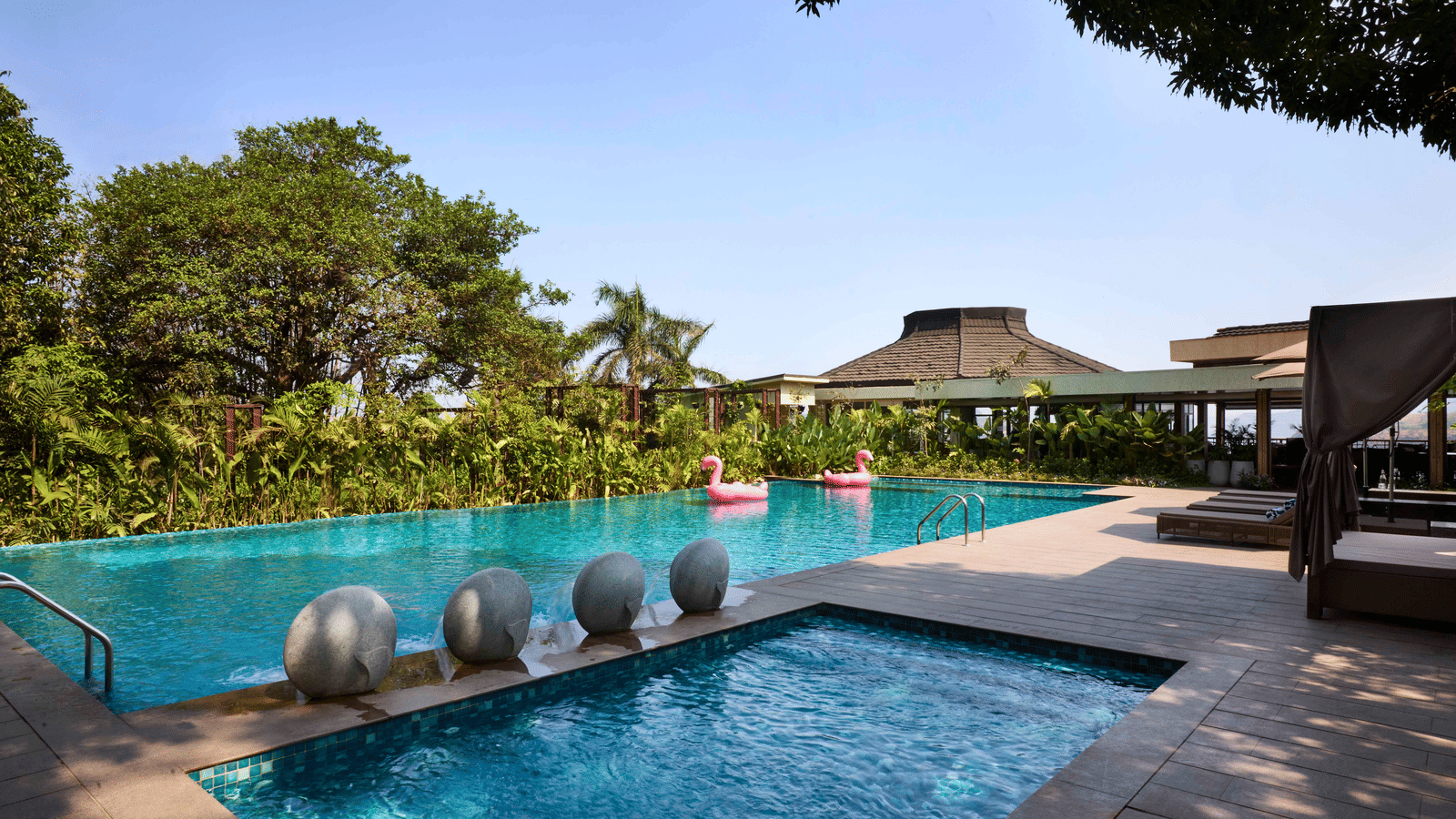 Outdoor luxury hotel swimming pool with a small wading area, bordered by dense greenery and architectural structures - Athiva Resort & Spa.