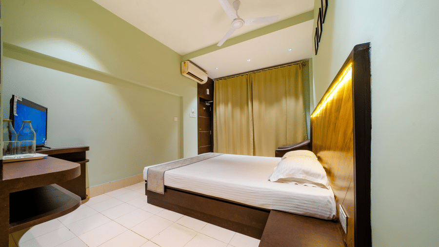 Hotel bedroom with a double bed, light green walls, and a flat-screen TV on a stand - Hotel Dolphin Puri